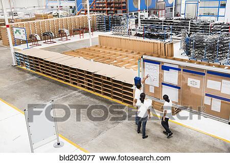 Stock Photo - Workers reading bulletin board in manufacturing plant. Fotosearch