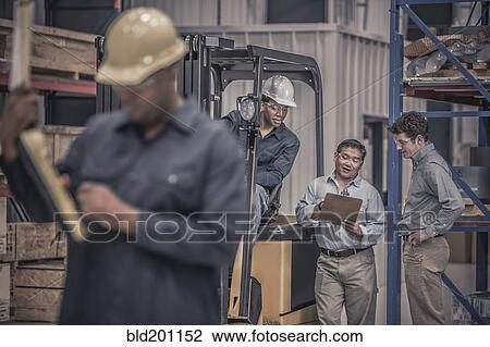 Stock Image - Workers talking together in factory. Fotosearch