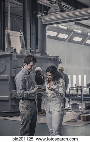 Stock Photography - Workers using digital tablet together in factory. Fotosearch