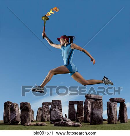 Stock Image - Athlete running with Olympic torch near Stonehenge. Fotosearch