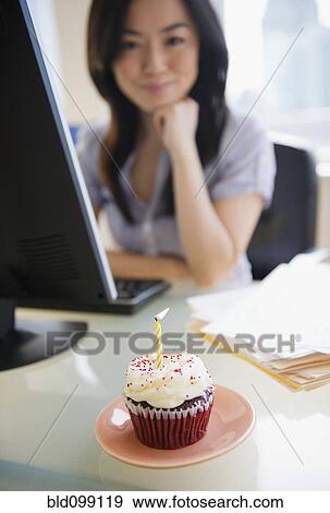 Birthday cupcake on desk near Japanese businesswoman View Large Photo Image Stock Photo - Birthday cupcake on desk near Japanese businesswoman. Fotosearch
