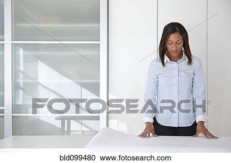 Stock Image - Black architect reviewing blueprints in office. Fotosearch