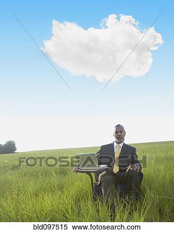 Stock Photography - Black businessman sitting at desk in field with laptop. Fotosearch