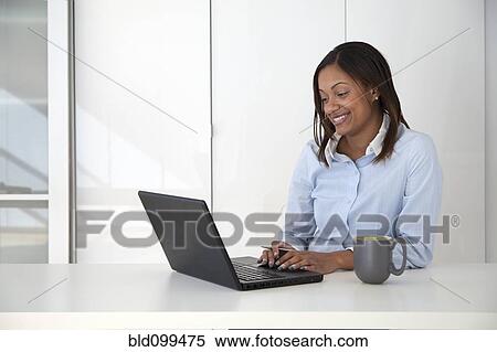 Stock Photography - Black businesswoman typing on laptop in office. Fotosearch