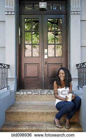 Stock Photograph - Black woman drinking coffee on front stoop. Fotosearch