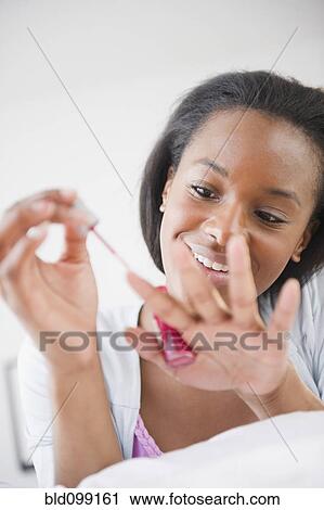 Stock Image - Black woman painting her fingernails. Fotosearch