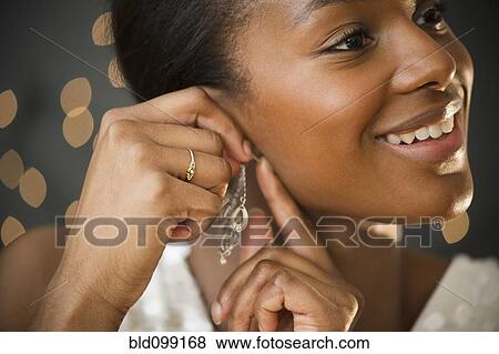 Stock Photo - Black woman putting on earring. Fotosearch