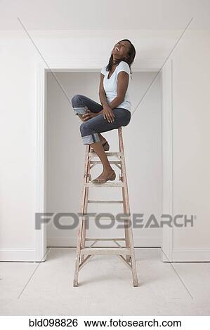 Stock Photograph - Black woman sitting on top of ladder. Fotosearch