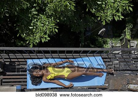 Stock Photo - Black woman sunbathing on fire escape. Fotosearch