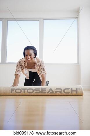 Stock Photo - Black woman unrolling carpet in new home. Fotosearch