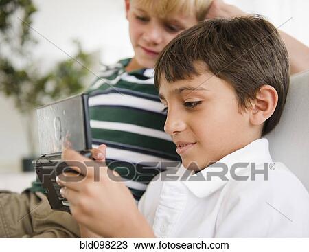 Stock Image - Boy watching friend playing hand-held video game. Fotosearch