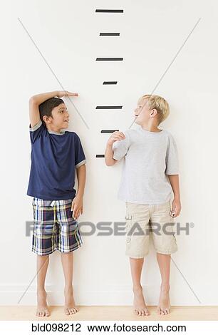 Stock Image - Boys measuring themselves against marks on wall. Fotosearch