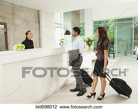 Stock Image - Business people arriving at hotel reception area. Fotosearch