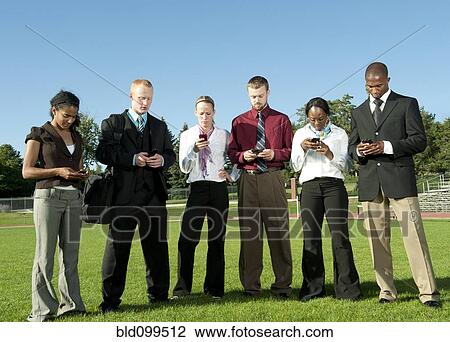 Stock Image - Business people standing in field text messaging on cell phones. Fotosearch