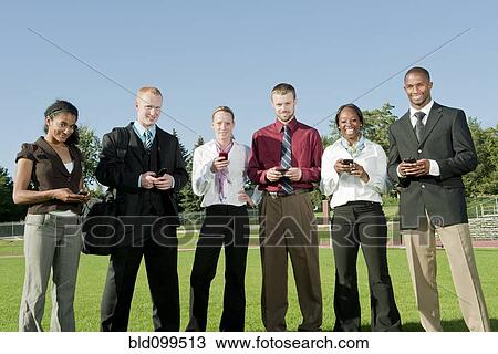 Stock Image - Business people standing in field text messaging on cell phones. Fotosearch