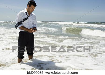 Businessman text messaging on cell phone while standing in ocean View Large Photo Image Stock Photography - Businessman text messaging on cell phone while standing in ocean. Fotosearch