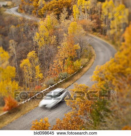 Stock Photography - Car driving along road through autumn leaves. Fotosearch
