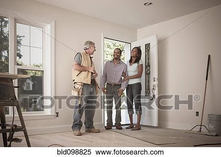 Stock Photography - Carpenter talking to couple in empty room. Fotosearch
