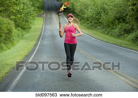 Stock Image - Caucasian athlete running with Olympic torch on remote road. Fotosearch