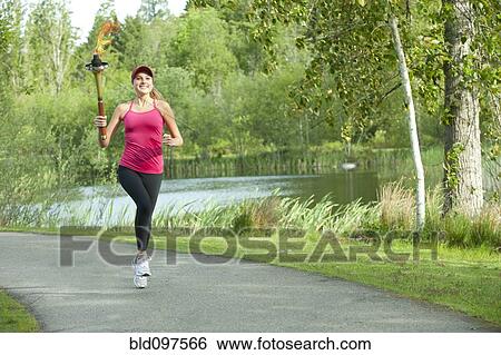 Stock Photograph - Caucasian athlete running with Olympic torch on park path. Fotosearch