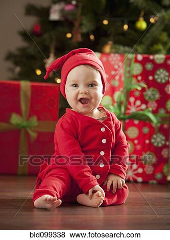 Stock Photo - Caucasian baby boy sitting near Christmas tree. Fotosearch