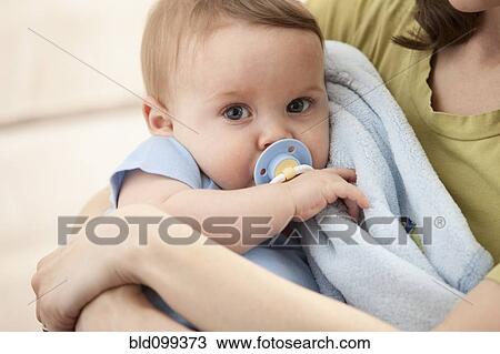Stock Image - Caucasian baby boy with pacifier in mother's arms. Fotosearch