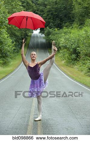 Stock Photograph - Caucasian ballerina dancing on remote road with umbrella. Fotosearch