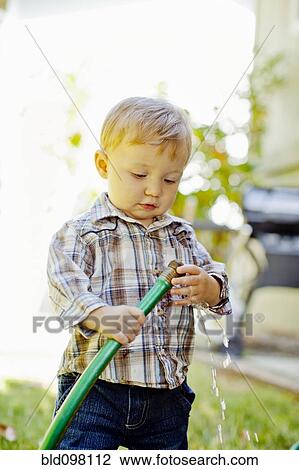 Stock Image - Caucasian boy playing with garden hose. Fotosearch