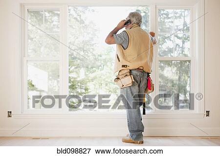 Stock Photo - Caucasian carpenter talking on cell phone in empty room. Fotosearch