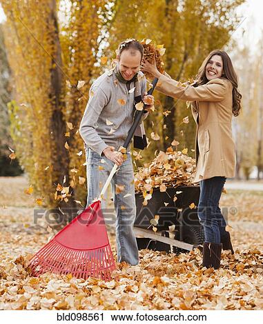 Stock Image - Caucasian couple raking autumn leaves. Fotosearch