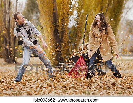 Stock Image - Caucasian couple raking autumn leaves. Fotosearch