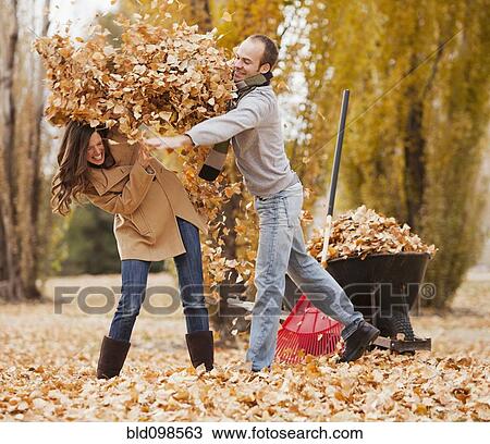 Stock Image - Caucasian couple raking autumn leaves. Fotosearch