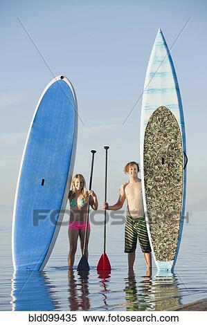 Stock Photography - Caucasian couple standing on beach with paddle boards. Fotosearch