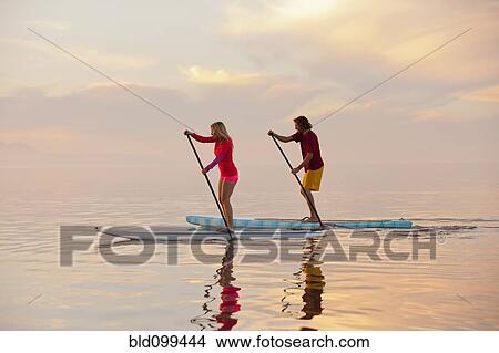 Picture - Caucasian couple standing on paddle boards. Fotosearch