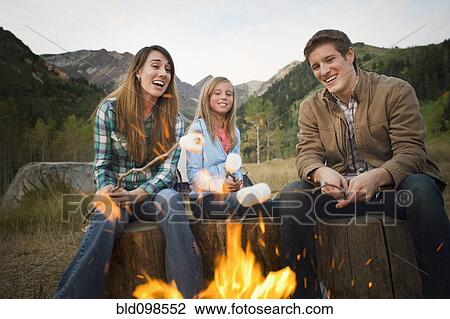 Stock Image - Caucasian family roasting marshmallows on campfire. Fotosearch