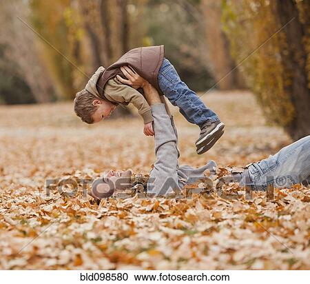 Stock Image - Caucasian father and son playing in autumn leaves. Fotosearch