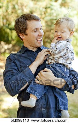 Stock Image - Caucasian father holding son outdoors. Fotosearch