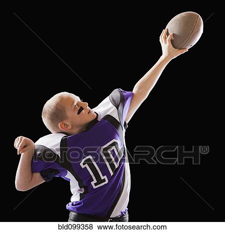 Stock Photo - Caucasian football player holding up football. Fotosearch