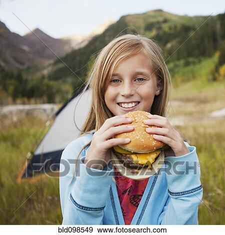 Stock Photo - Caucasian girl eating cheeseburger at campsite. Fotosearch
