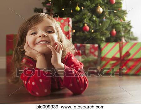 Stock Photo - Caucasian girl laying on floor near Christmas tree. Fotosearch
