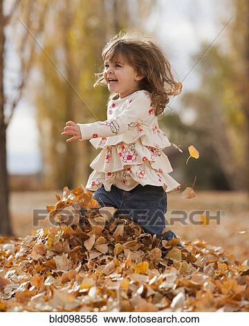 Stock Photograph - Caucasian girl playing in autumn leaves. Fotosearch