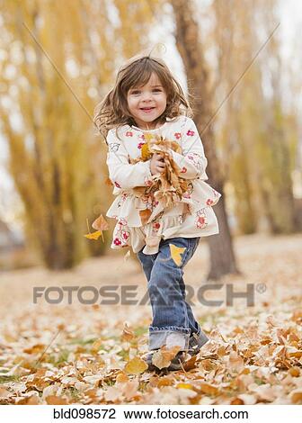 Stock Image - Caucasian girl playing with autumn leaves. Fotosearch