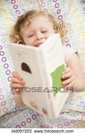 Stock Image - Caucasian girl reading book in bed. Fotosearch