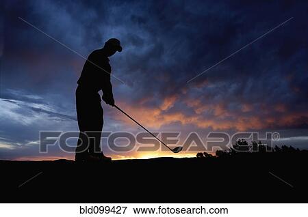 Stock Photo - Caucasian golfer swinging golf club at sunset. Fotosearch