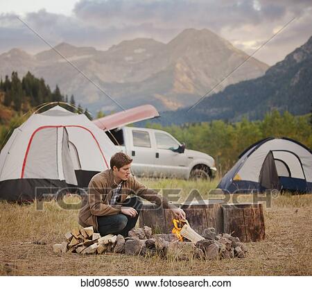 Stock Image - Caucasian man building campfire at campsite. Fotosearch