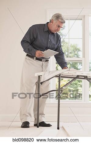 Caucasian man holding digital tablet looking at blueprint View Large Photo Image Stock Image - Caucasian man holding digital tablet looking at blueprint. Fotosearch