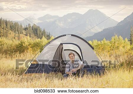 Stock Image - Caucasian man sitting in tent. Fotosearch