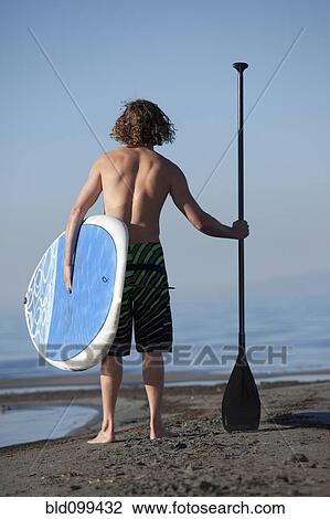 Caucasian man standing on beach with paddle board View Large Photo Image Stock Image - Caucasian man standing on beach with paddle board. Fotosearch