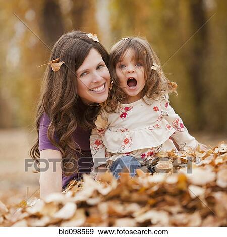 Stock Photo - Caucasian mother and daughter playing in autumn leaves. Fotosearch