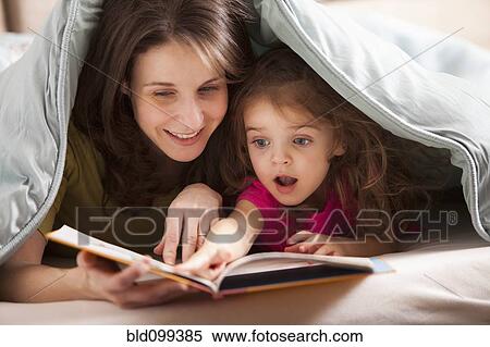 Stock Photography - Caucasian mother and daughter reading book under covers. Fotosearch